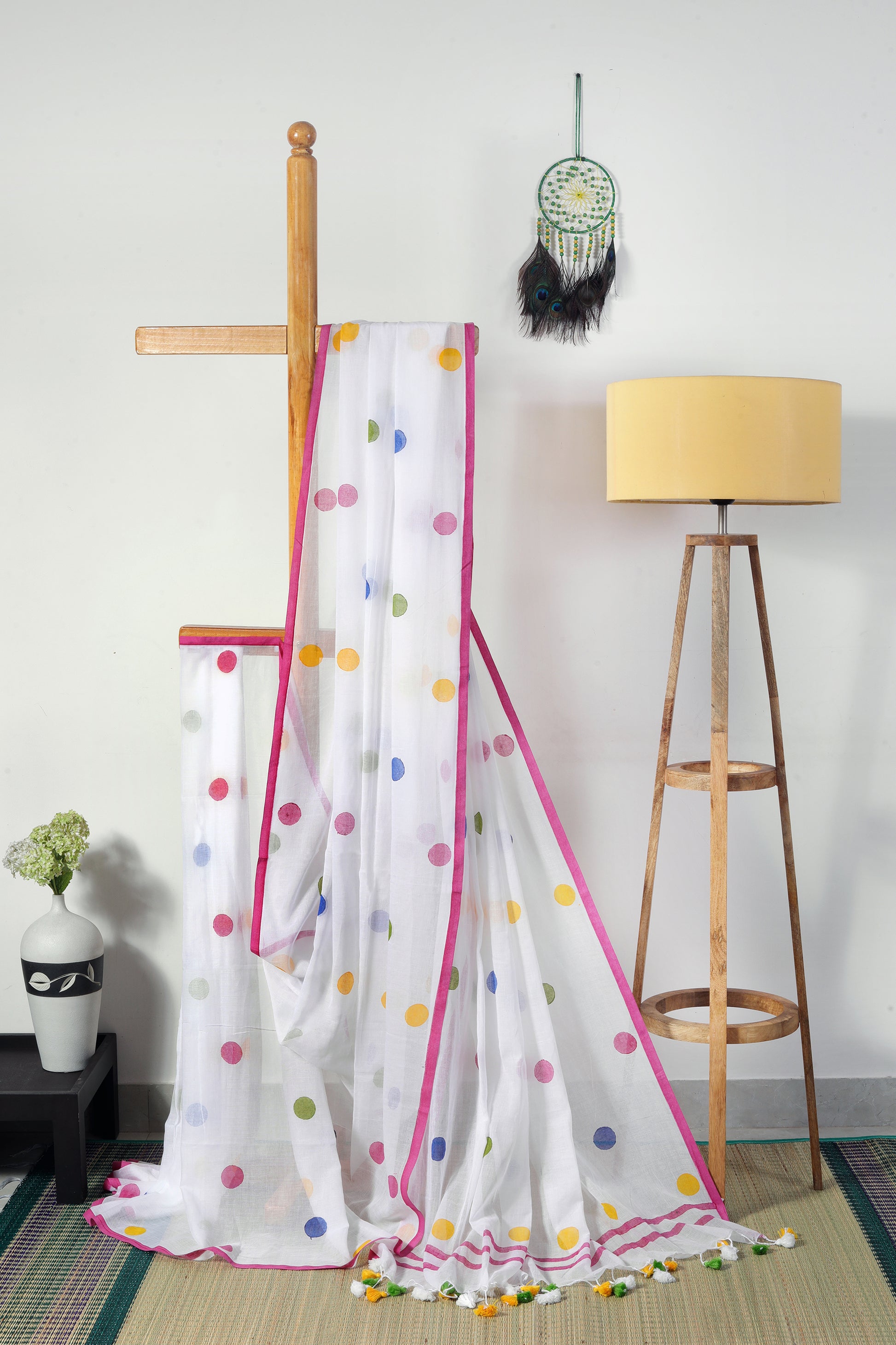 this saree is a breezy celebration of playfulness and poise. this milky white mul cotton saree is dotted with large, vibrant polka dots with a cheerful pink border and colorful tassels