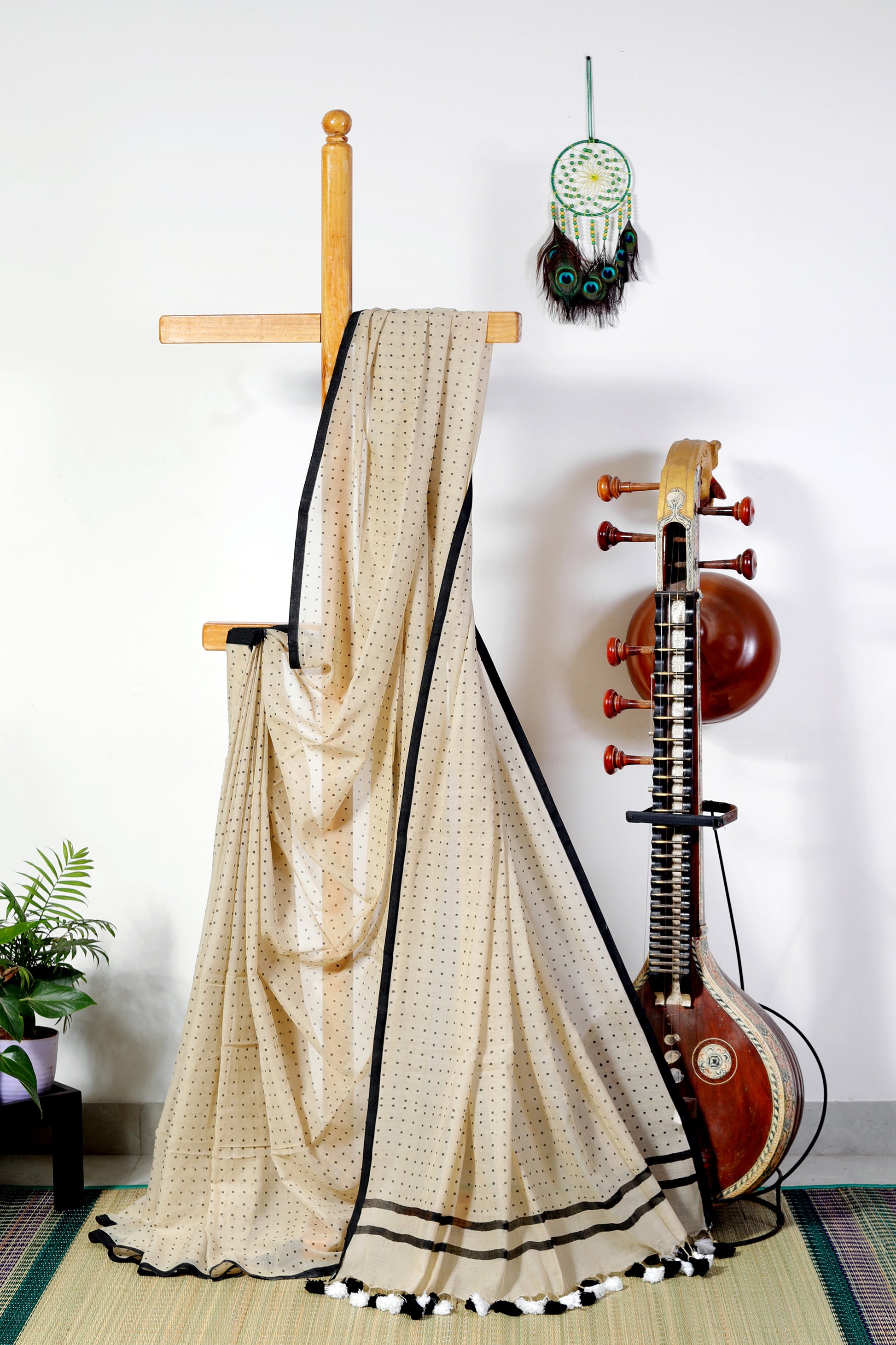 A soft beige mul cotton saree, light as a whisper and airy like a breeze. Scattered across its canvas are delicate black bindi-like polka dots — subtle, playful, and timeless