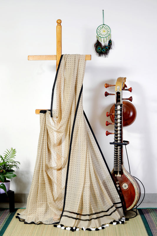 A soft beige mul cotton saree, light as a whisper and airy like a breeze. Scattered across its canvas are delicate black bindi-like polka dots — subtle, playful, and timeless